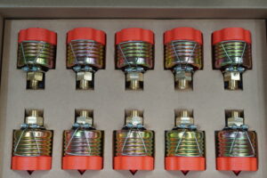 Five identical metal compression springs with red plastic end caps, secured by blue wires, arranged in a cardboard tray.